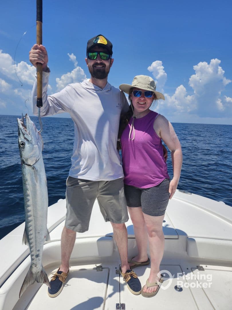 Two anglers proudly displaying a Barracuda caught during a sunny day on the water.