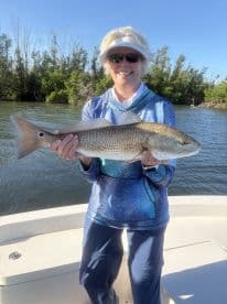 An angler proudly displaying a large Redfish while fishing in a scenic coastal environment.