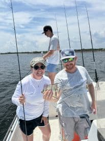 Two anglers proudly displaying a caught fish while fishing on a boat, with a scenic backdrop of water and sky.