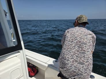 An angler actively reeling in a catch while fishing on a boat in open water, showcasing the excitement of the fishing experience.