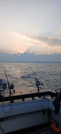 A serene view from the helm of a fishing boat at sunset, showcasing fishing rods ready for action on the open water.