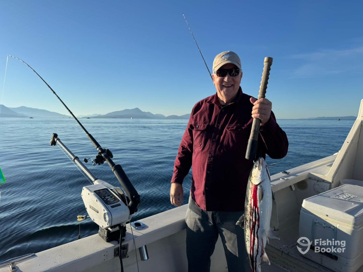 An angler proudly displaying a freshly caught fish while on a boat in calm waters, surrounded by mountains in the background.
