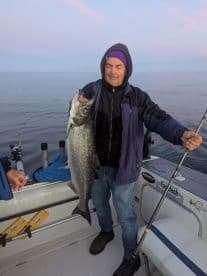 An angler proudly displaying a large Lake Michigan Salmon while fishing on a boat during a serene morning.