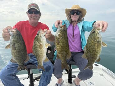 Two anglers proudly displaying their catch of four large Smallmouth Bass while enjoying a day on the water.