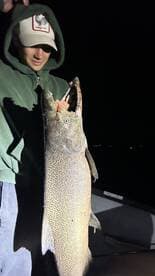 A young angler proudly displaying a large salmon caught during a night fishing trip.
