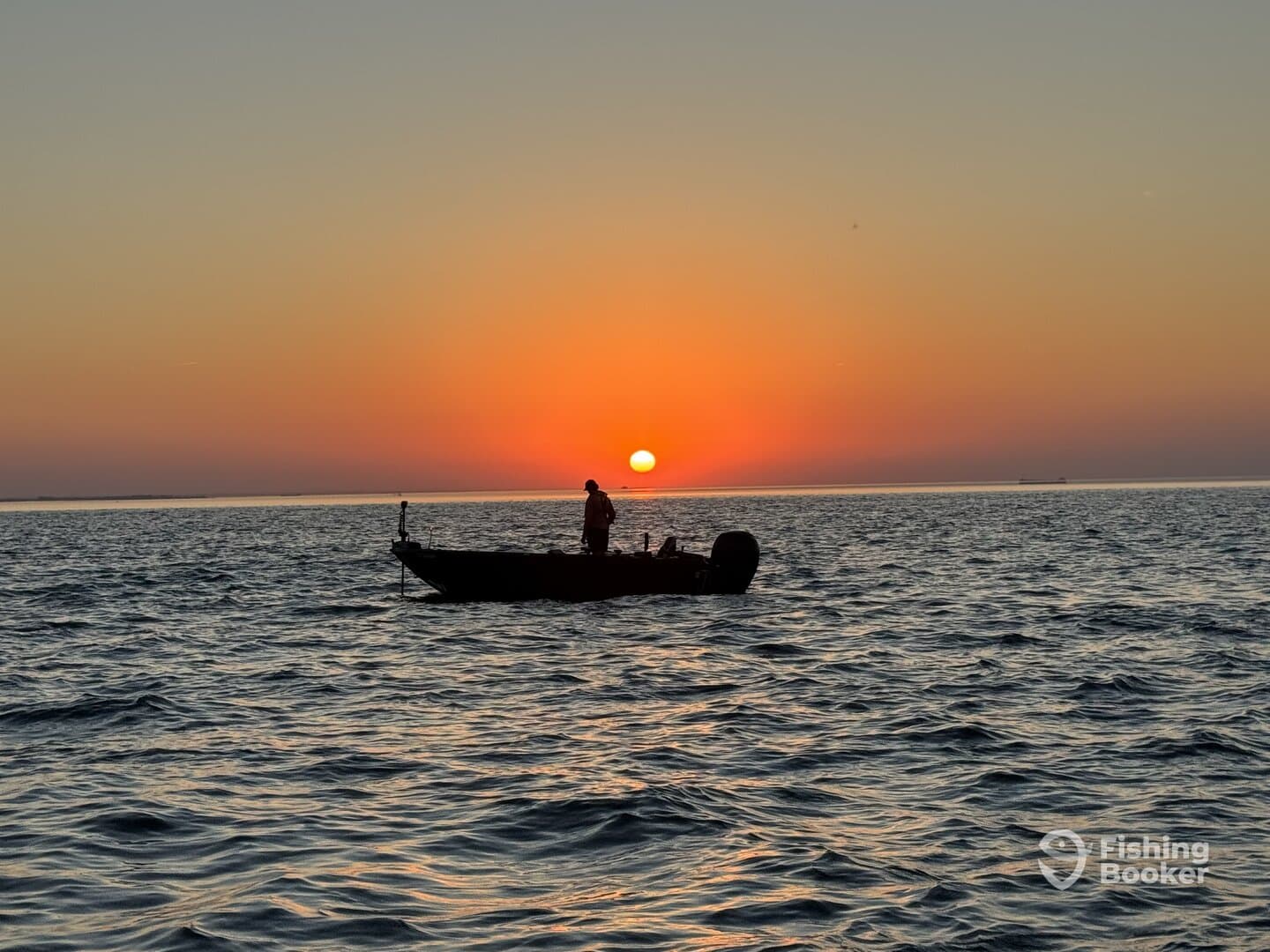 A lone angler stands on a small boat silhouetted against a stunning sunset over the ocean, creating a serene fishing atmosphere.