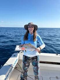 Angler proudly displaying a colorful fish while aboard a fishing boat in open waters, showcasing a successful day of fishing.