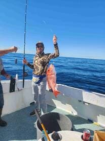 Angler proudly displaying a large Red Snapper while fishing on a charter boat in open waters.