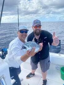 Two anglers proudly displaying a large fish while on a fishing charter in open waters.