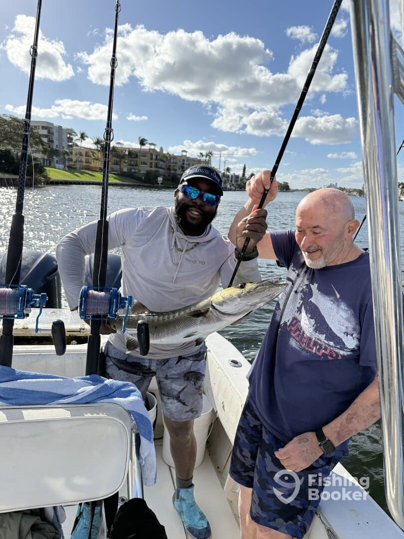 Two anglers celebrating a successful catch of a large Snook while fishing from a boat in a scenic waterway.