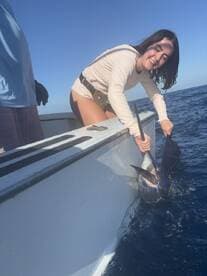 Angler smiling while reeling in a large fish, likely a Marlin, during a deep-sea fishing trip.