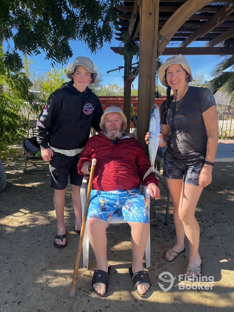 A family poses proudly with a large fish after a successful fishing trip, showcasing their catch in a sunny outdoor setting.