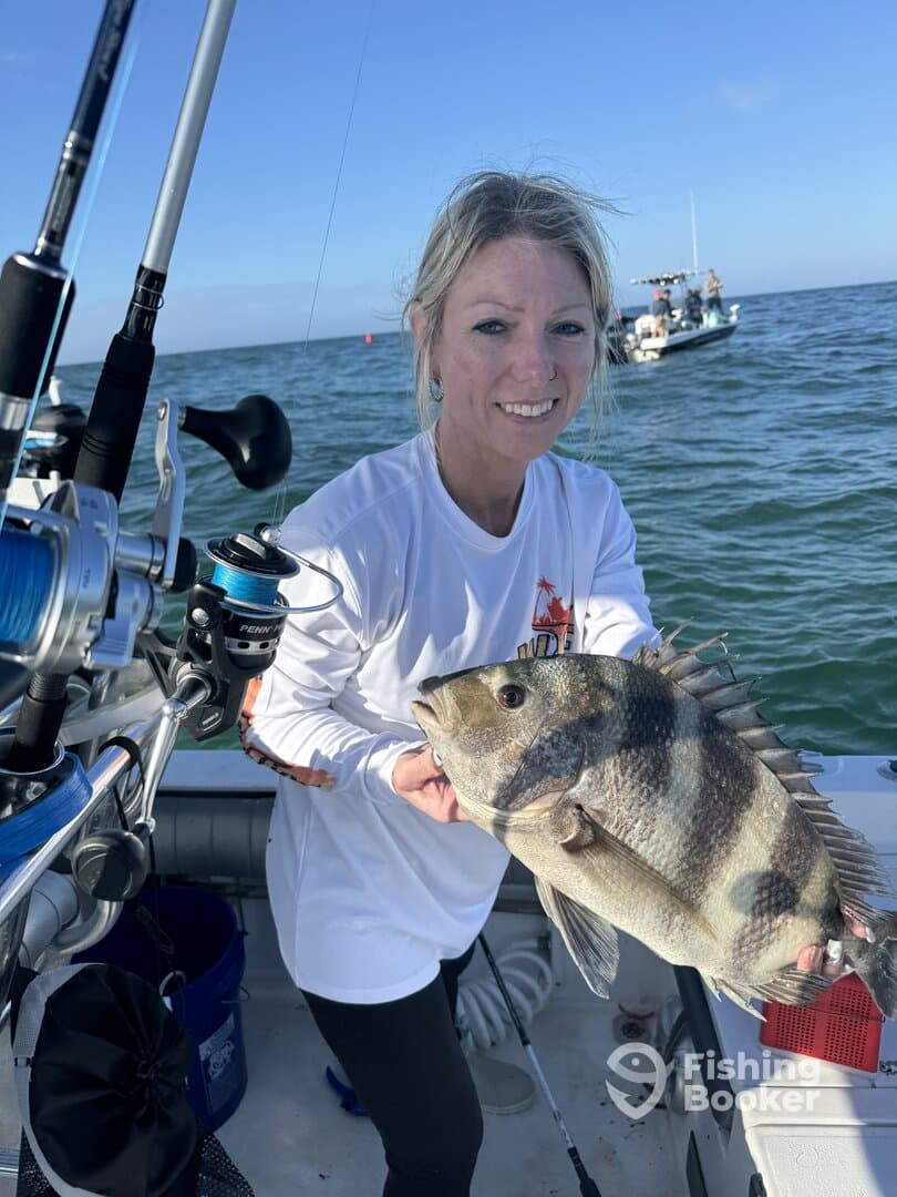 Angler proudly displaying a large Black Drum while fishing on a sunny day, with another boat visible in the background.