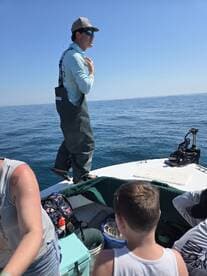 A young boy and an adult are engaged in fishing activities on a boat, with calm waters in the background, showcasing a family fishing experience.