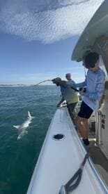 A young angler is reeling in a shark while fishing off the coast, showcasing an exciting moment on the water.