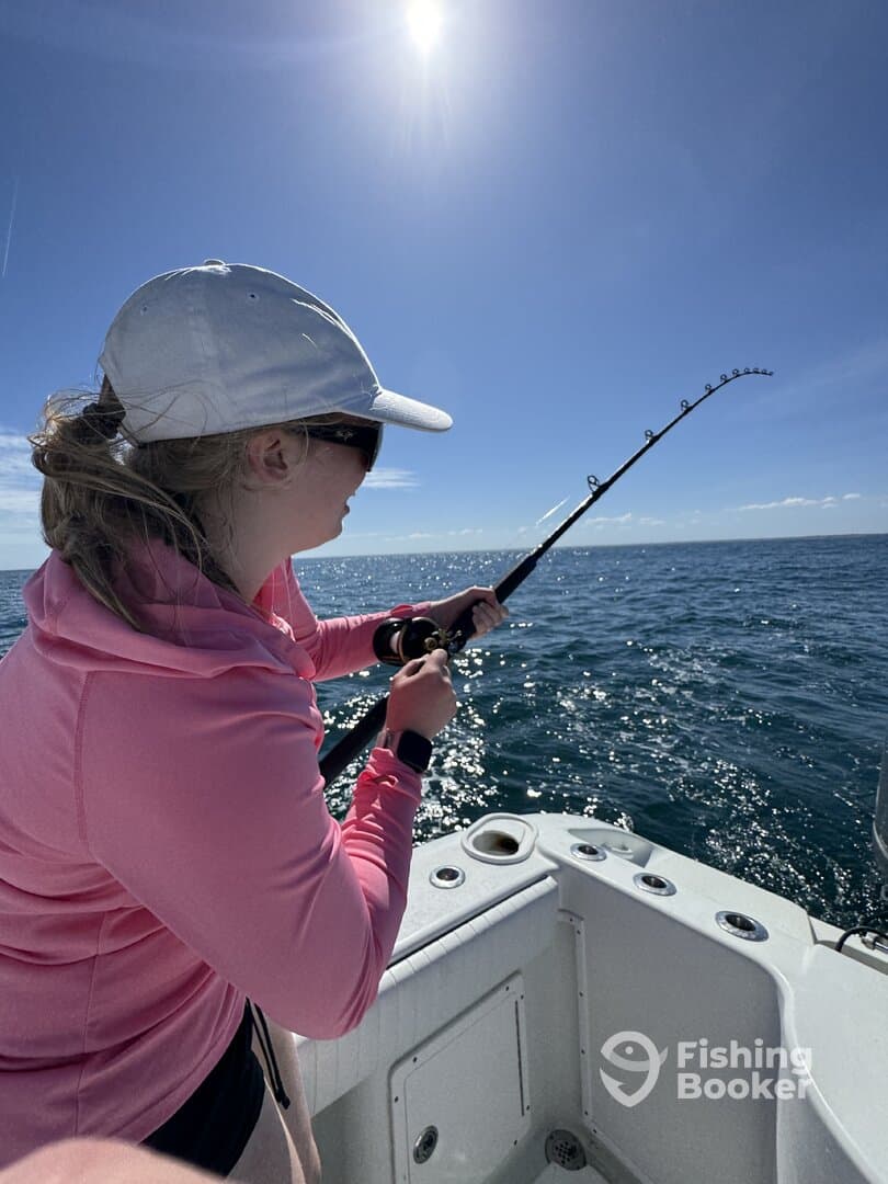 A young angler is actively reeling in a fish while fishing on a sunny day, showcasing the excitement of the sport.