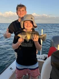 Two young anglers proudly displaying a caught fish while enjoying a day on the water.