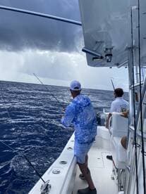 Anglers actively fishing on a boat in open waters, with overcast skies creating a dramatic backdrop.