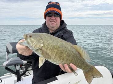 Angler proudly displaying a sizable Smallmouth Bass while fishing on a boat in open water.
