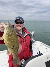 Angler proudly displaying a large Smallmouth Bass while fishing on a boat, showcasing a successful day on the water.