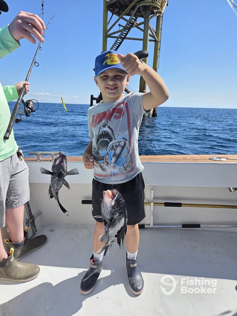 A young angler proudly displaying two caught fish while fishing near an offshore platform, showcasing a fun family fishing experience.