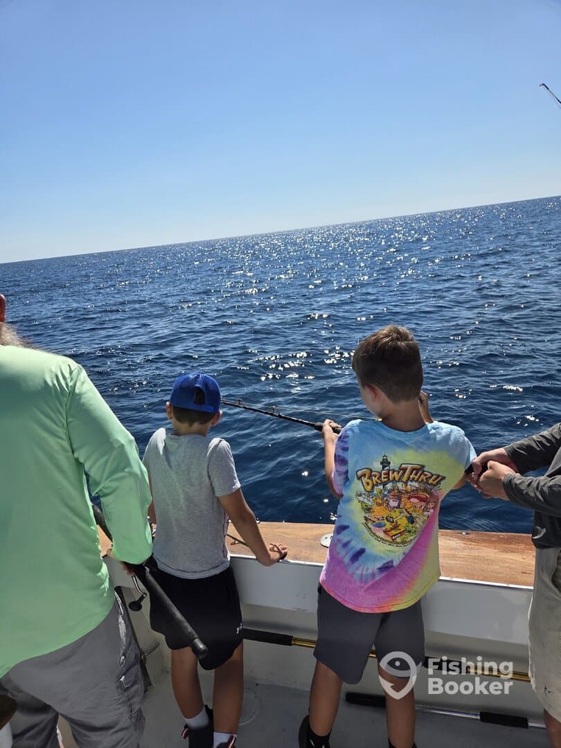 Two young anglers actively reeling in their lines while fishing on a sunny day at sea.