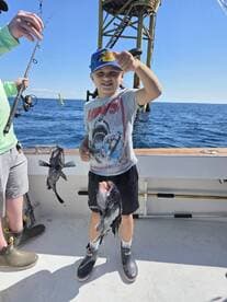 A young angler proudly displaying two caught fish while fishing near an offshore platform, showcasing a fun family fishing experience.