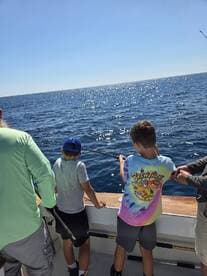 Two young anglers actively reeling in their lines while fishing on a sunny day at sea.