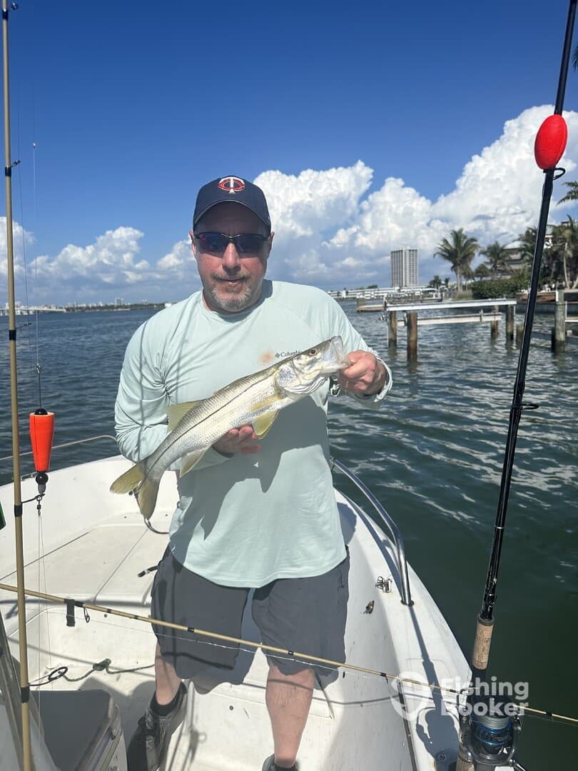 Angler proudly displaying a large Snook while fishing from a boat in a scenic coastal environment.