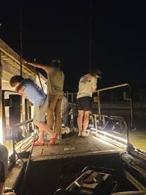 A group of anglers fishing at night from a boat, illuminated by lights, creating an exciting atmosphere for catching fish.
