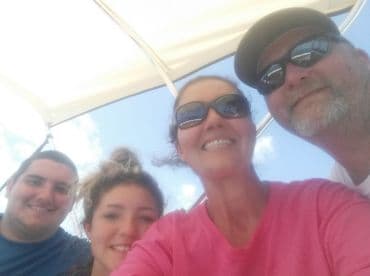 A cheerful group of four enjoying a sunny day on a boat, capturing a selfie while relaxing on the water.