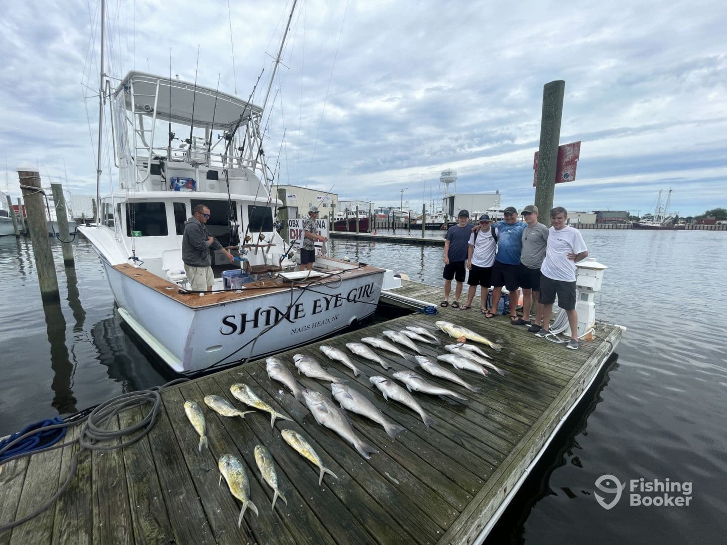 A group of anglers posing with their catch of various fish, including Mahi Mahi and Snapper, displayed neatly on the dock next to the 'Shine Eye Girl' charter boat in Nags Head, NC.