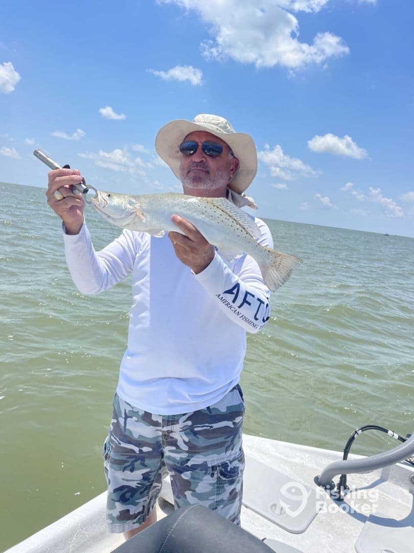 An angler proudly displaying a Speckled Trout while fishing on a sunny day in coastal waters.