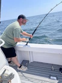An angler actively reeling in a fish while fishing on a boat in open water, showcasing the excitement of the catch.