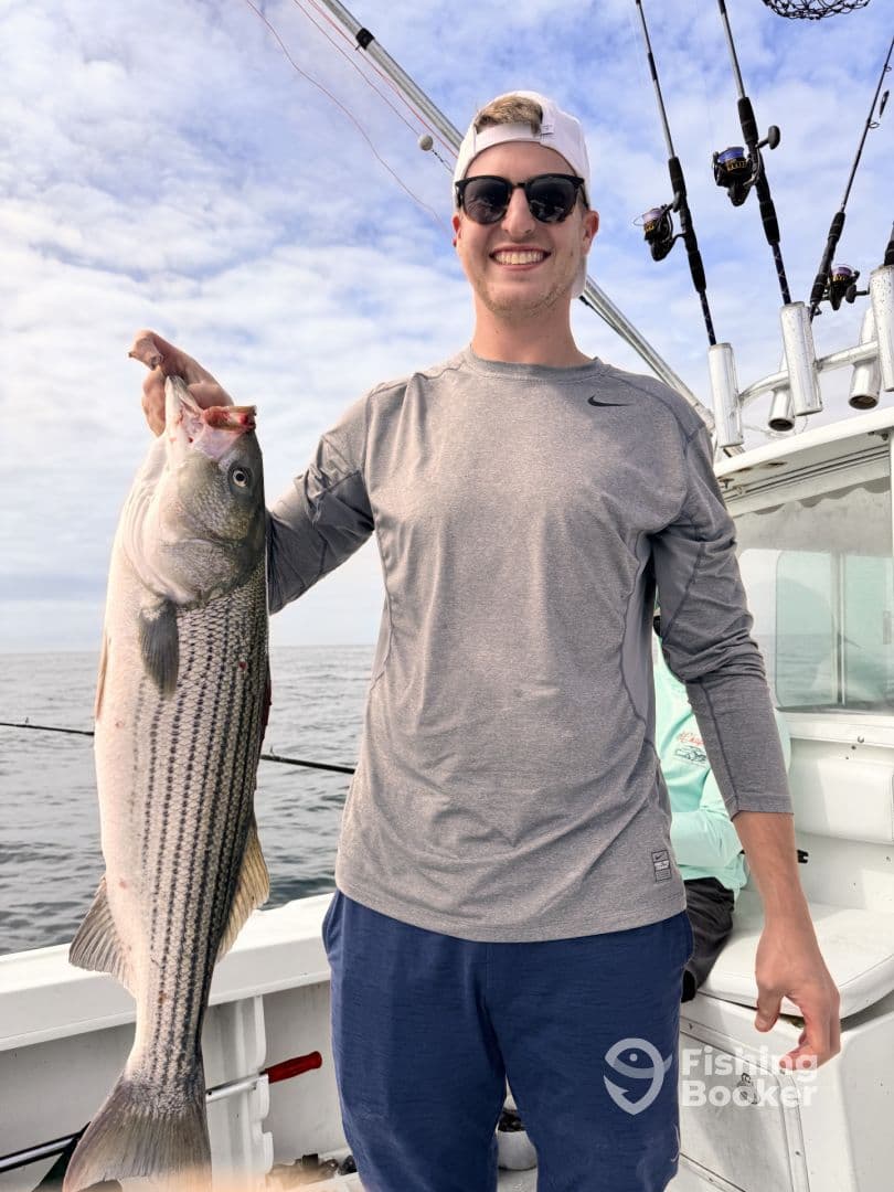Angler proudly displaying a large Striped Bass while fishing on a charter boat.