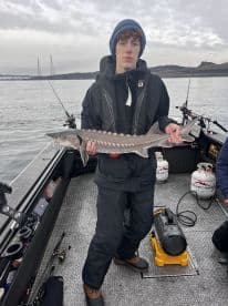 A young angler proudly displaying a Sturgeon while fishing from a boat, showcasing the excitement of a successful catch.
